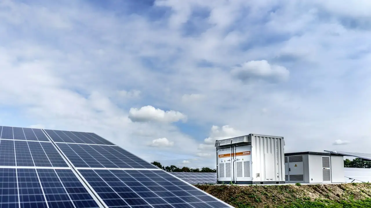 Solarmodule im Freifeld mit Container-Speichern im Hintergrund unter bewölktem Himmel
