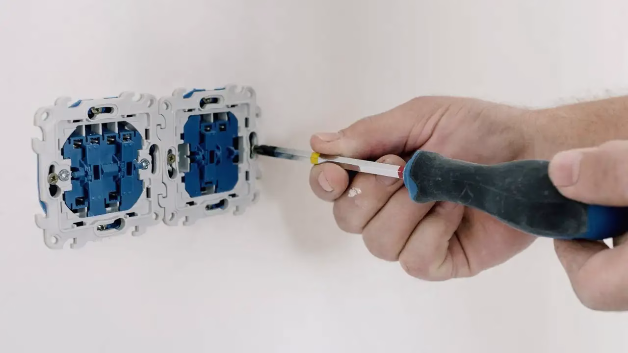 Hand mit Schraubenzieher an zwei ausgebauten Steckdosen an einer weissen Wand Hand mit Schraubenzieher an zwei ausgebauten Steckdosen an einer weissen Wand
