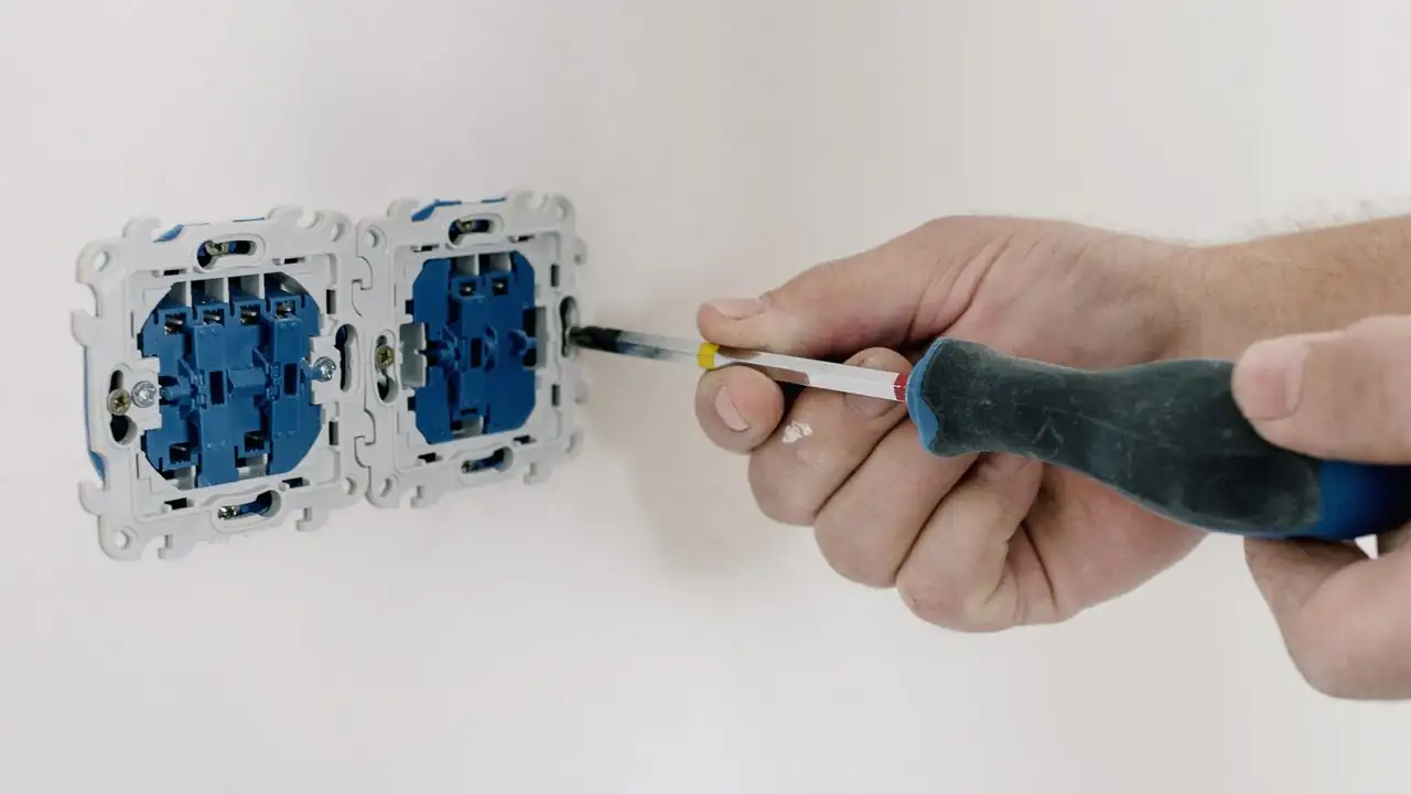 Hand mit Schraubenzieher an zwei ausgebauten Steckdosen an einer weissen Wand