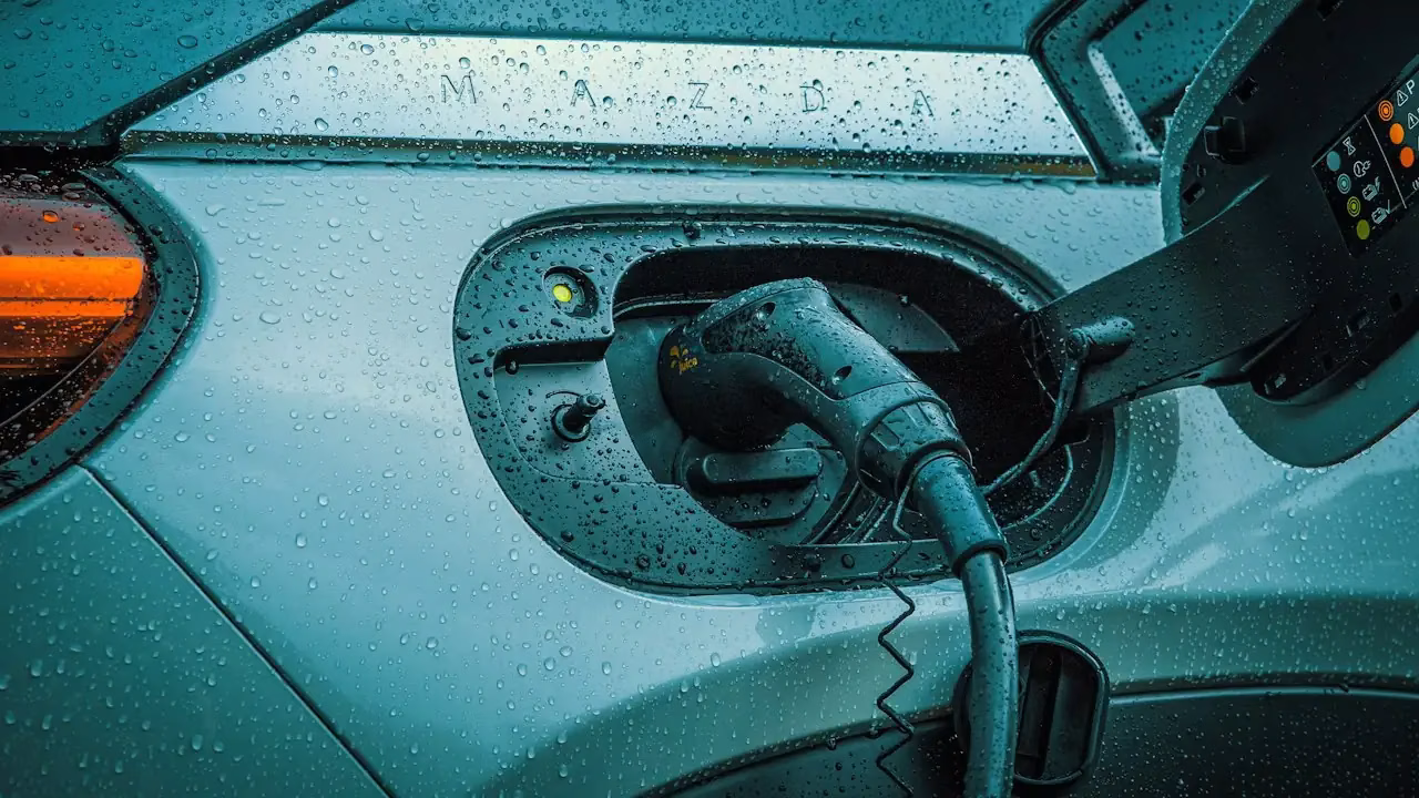Ladestecker im Ladeanschluss eines Autos, Wassertropfen auf der Karosserie Ladestecker im Ladeanschluss eines Autos, Wassertropfen auf der Karosserie