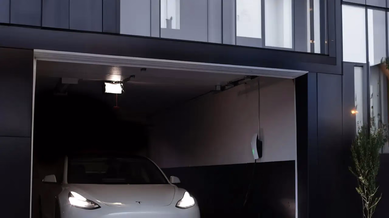 Weisses Elektroauto mit eingeschalteten Scheinwerfern in einer Garage eines modernen Hauses Weisses Elektroauto mit eingeschalteten Scheinwerfern in einer Garage eines modernen Hauses