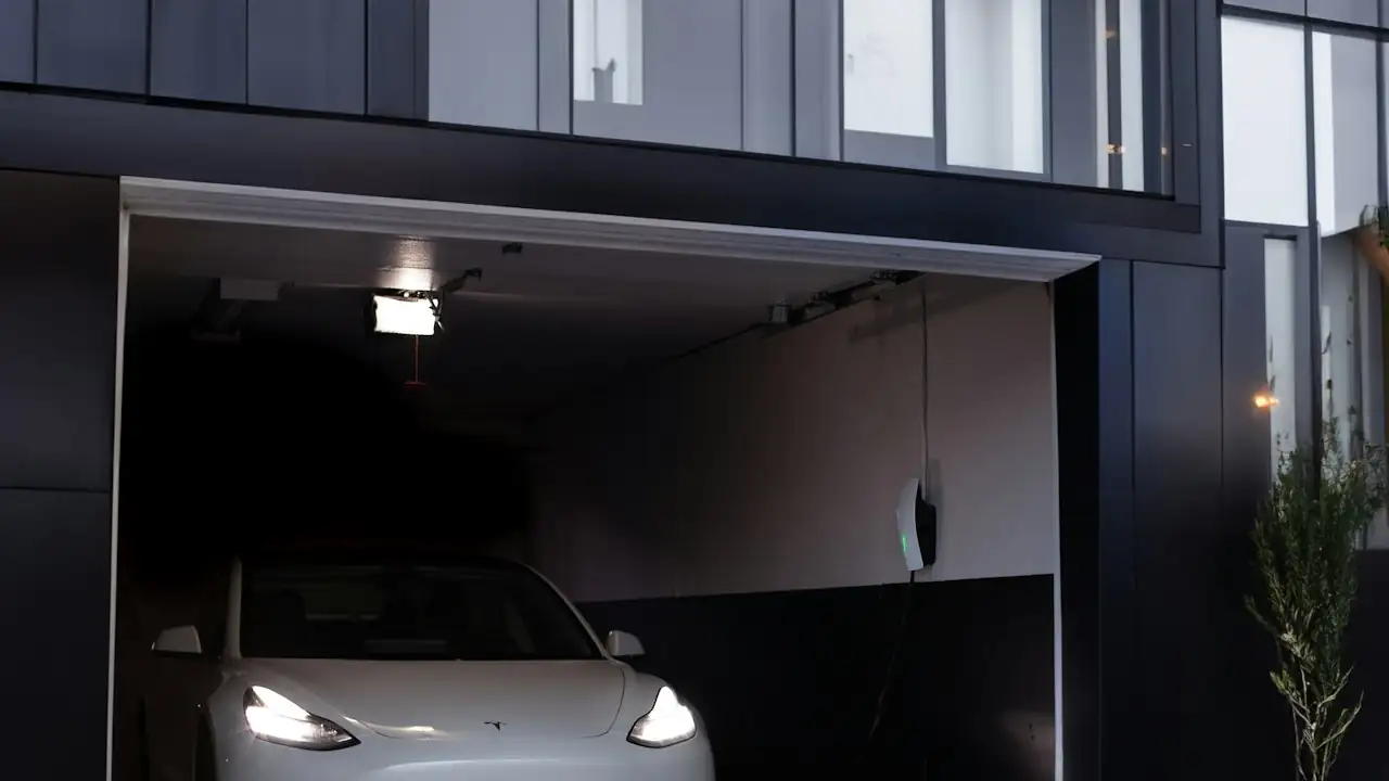 Weisses Elektroauto mit eingeschalteten Scheinwerfern in einer Garage eines modernen Hauses
