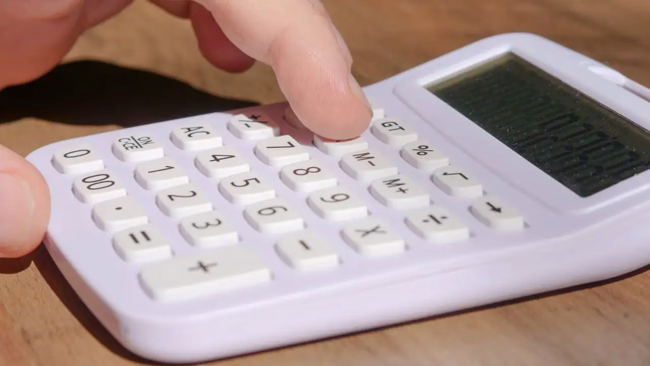 Finger tippen auf einen weissen Taschenrechner auf einem Holztisch