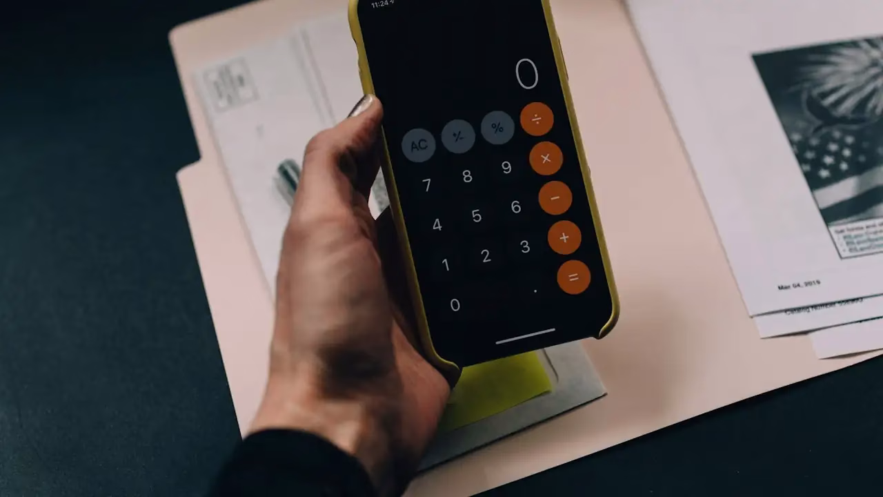 Hand hält ein Smartphone mit Taschenrechner-App über Unterlagen