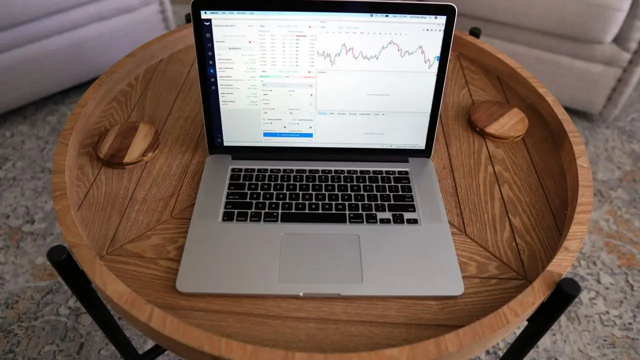 Laptop mit Börsenchart auf einem runden Holztisch von oben gesehen
