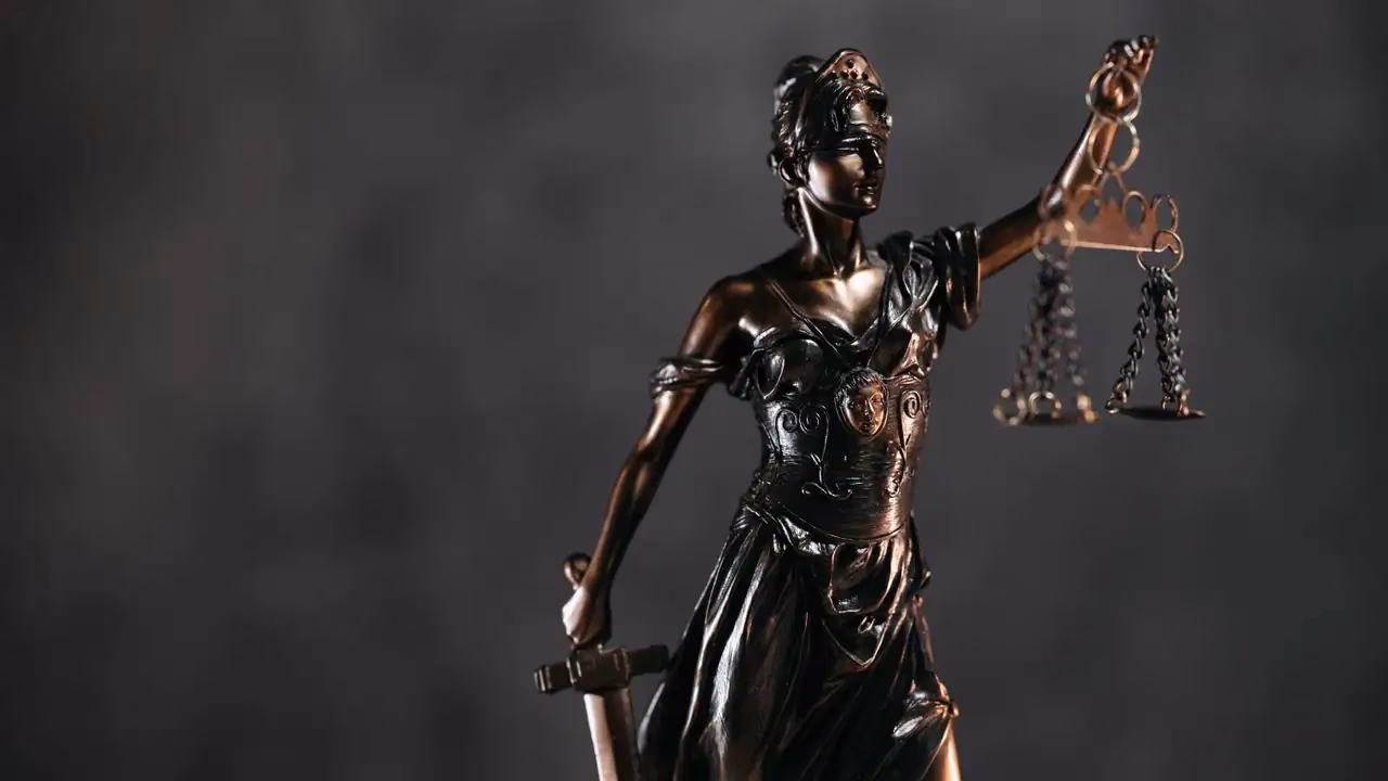 Bronzestatue der Justitia mit erhobener Waage vor dunklem Hintergrund