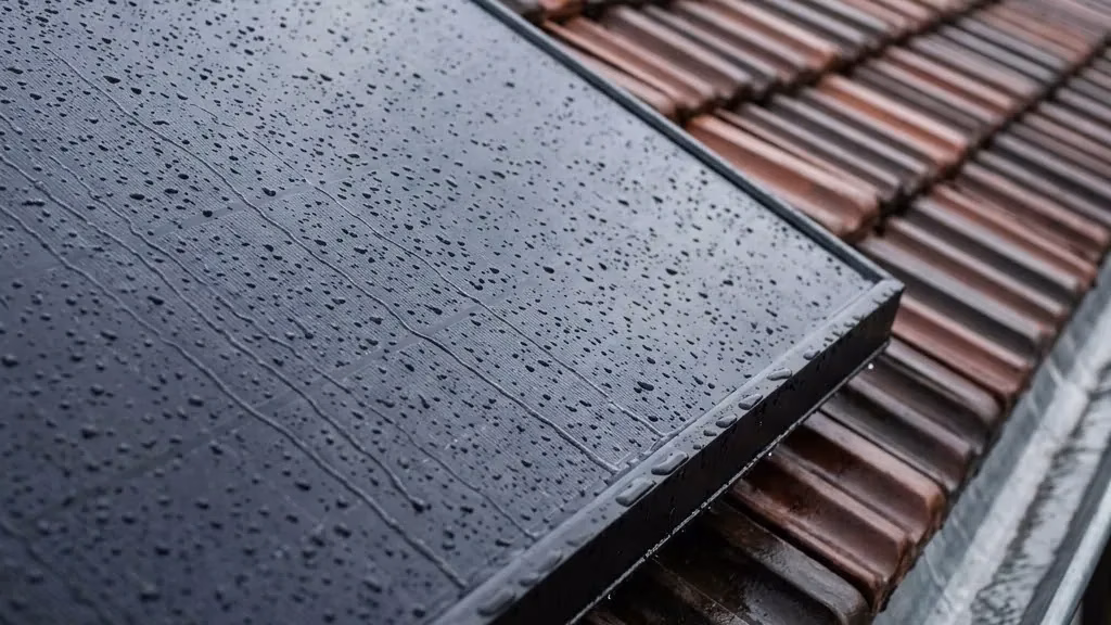 Regentropfen perlen auf der Glasfläche eines Solarmoduls auf dem Ziegeldach