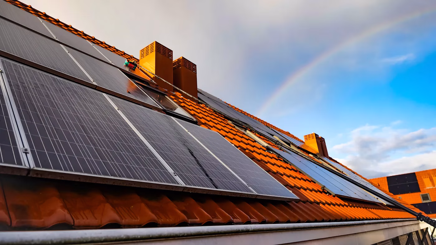 Solarmodule auf einem Ziegeldach mit Regenbogen im Hintergrund
