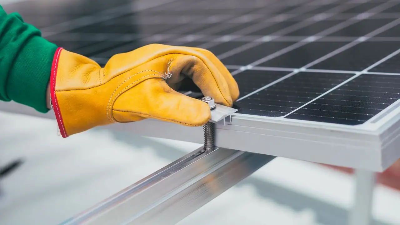 Handschuh befestigt die Halterung eines Solarmoduls am Montageprofil