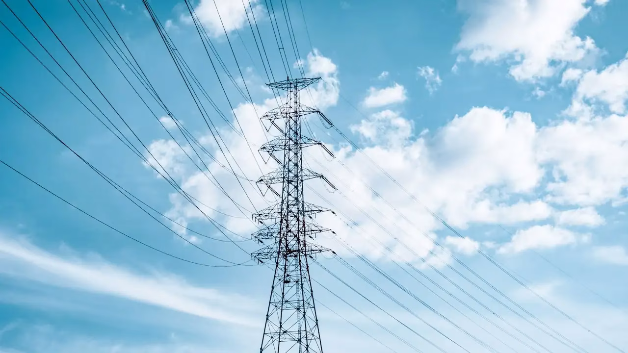 Hochspannungsmast mit Leitungen vor blauem Himmel mit Wolken