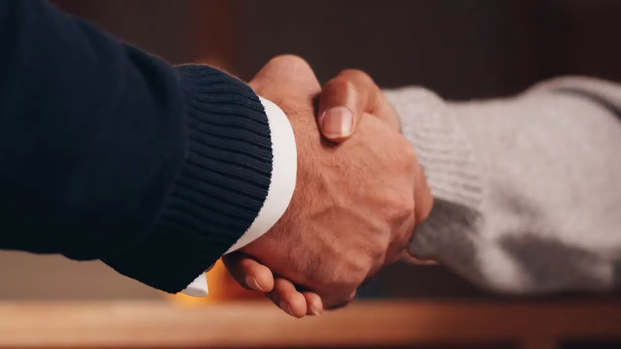 Nahaufnahme eines Handschlags zwischen zwei Personen in dunklem Pullover und grauem Strick