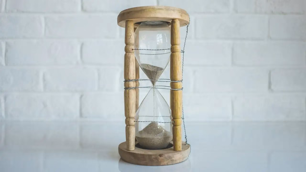 Sanduhr mit Holzrahmen vor einer weissen Backsteinwand